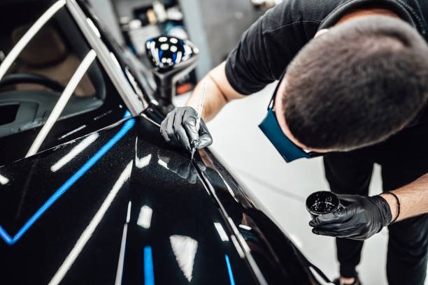 Professional worker fixing luxury car scratches at car detailing and valeting service center.