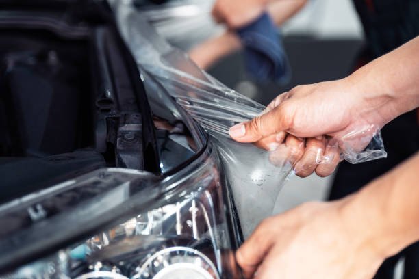 Man pealing the transparent insulation from the black car